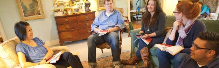 Several people seated in a semi-circle facing each other enjoying a small group bible study in a private home living room setting