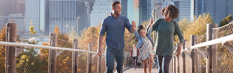 A woman dating as a single parent brings her daughter on a date, and as they cross a city bridgeway, the couple holds the young girl's hands while she happily skips along with the them.