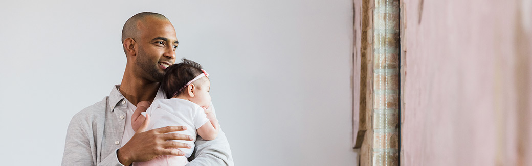 A father holds his infant daughter on his shoulder and pats the baby's back to comfort her, taking on one of the many roles of a father