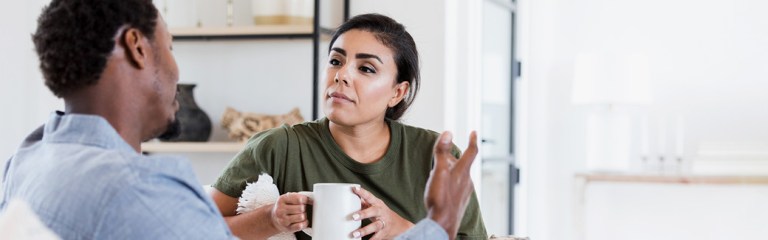 A married couple in their home relaxing with a cup of coffee and having a conversation